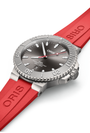 The Oris Aquis Date Relief dive watch, featuring a grey dial and a red rubber strap, is displayed at an angle on a white background.