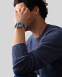 A man in a blue sweater covers part of his face with his hand, showcasing the Zenith Chronomaster Original blue-faced wristwatch.