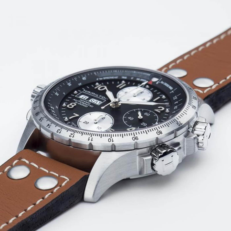 A close-up of the Hamilton Khaki Aviation X-Wind Auto Chrono showcases its black dial with three subdials, silver case, and brown leather strap with white stitching, emphasizing its automatic movement and aviation-inspired design.