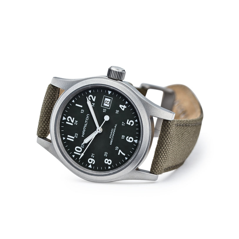 The Hamilton Khaki Field Mechanical wristwatch features a black dial with white numerals and an olive green fabric strap, displayed at an angle.