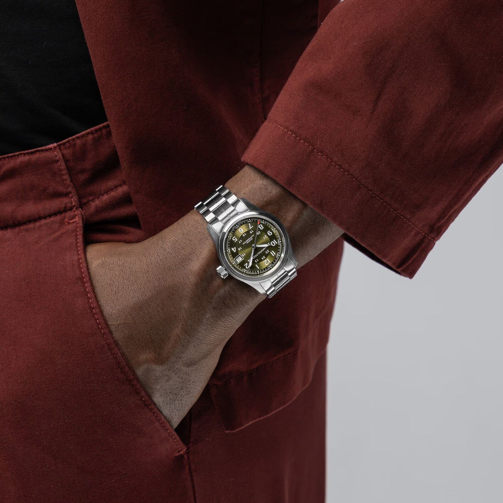 A person in a red outfit has their left hand, wearing a Hamilton Khaki Field Auto 38mm watch, in their pocket.