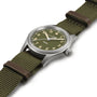 The Hamilton Khaki Field Quartz 33mm boasts a durable design with an olive dial, khaki fabric strap, Arabic numerals, and a silver case, all reflecting classic military heritage and set against a white background.