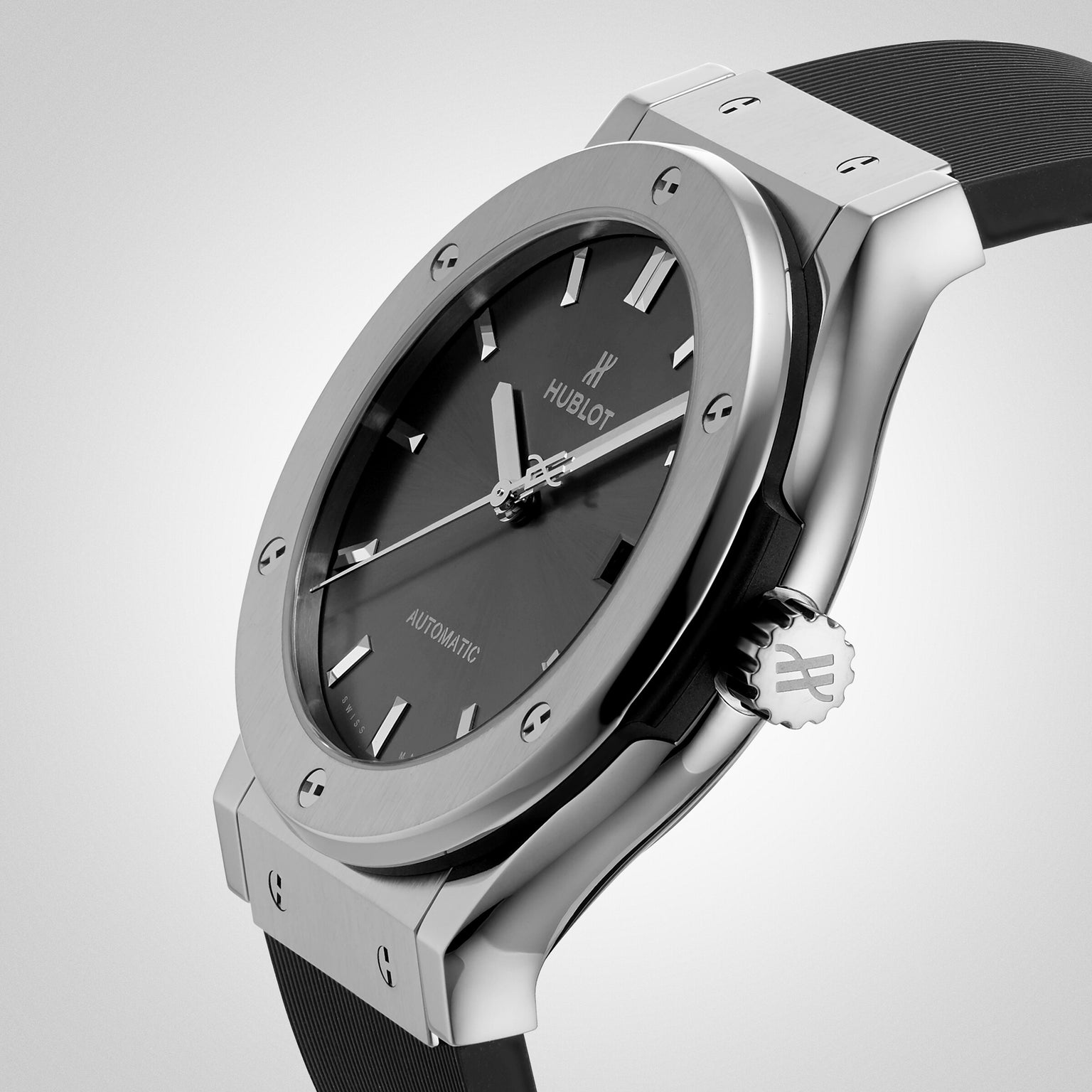 A close-up of the Hublot Classic Fusion Racing Grey Titanium wristwatch, showcasing its titanium case, black dial, black rubber strap, and self-winding movement with the time set to 10:10.