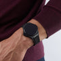 A person wearing a Hublot Big Bang E Gen3 Black Magic smartwatch with a blank screen on their left wrist, paired with a maroon long-sleeve sweater.