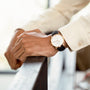 A person wearing a cream shirt and a Girard-Perregaux 1966 40 wristwatch rests their hand on a railing.