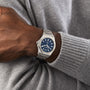 A person wearing a Girard-Perregaux Laureato 42 wristwatch with a blue dial, silver hour markers, and an octagonal bezel, styled in a gray sweater.