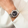 A person wears the Girard-Perregaux Laureato 42, a silver wristwatch with an octagonal bezel, black dial, 42mm stainless steel case, and metal band on their left wrist over a white long-sleeve shirt.