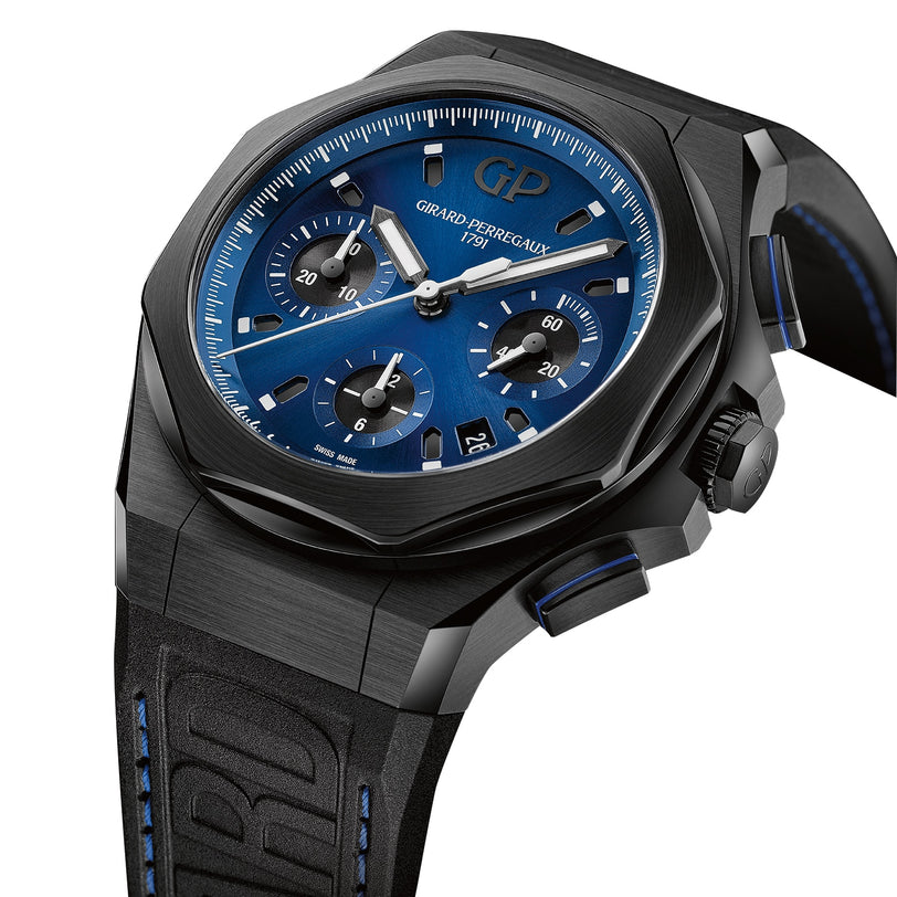 The Laureato Absolute Chronograph by Girard-Perregaux features a black PVD titanium case, blue dial with three sub-dials and date display, plus a black rubber strap with blue stitching, shown against a white background.