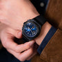 A person in a brown jacket checks a Girard-Perregaux Laureato Absolute Chronograph with a black PVD-treated titanium case and black strap on their left wrist.