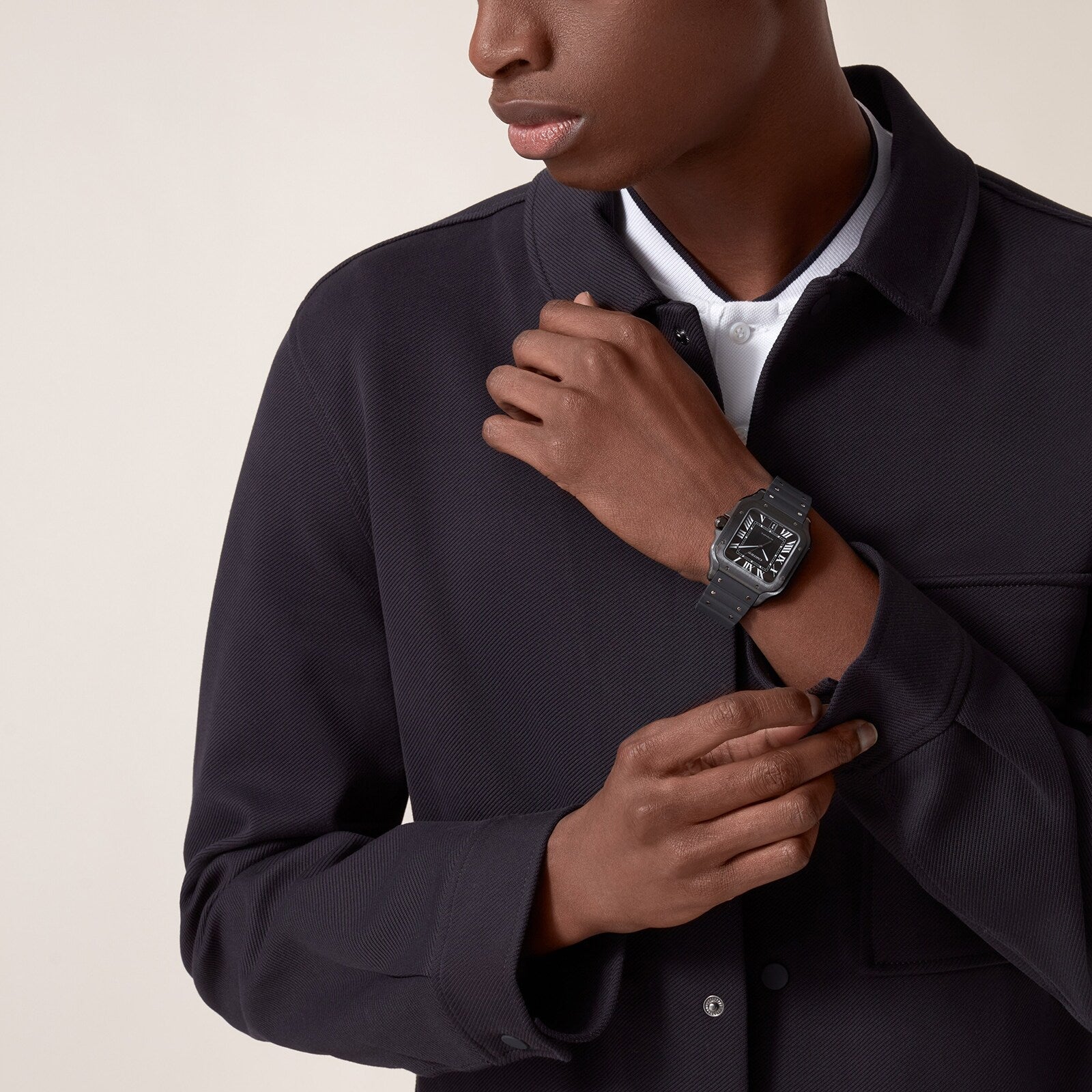 A person in a dark jacket adjusts their sleeve, showcasing the square black Santos de Cartier watch by Cartier against a plain background.