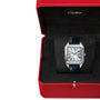 A Cartier Santos-Dumont watch with mechanical movement, blue leather strap, and Roman numeral dial is shown in an open red Cartier box with black interior.