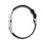 Side view of the Cartier Santos-Dumont watch with a blue gemstone crown, mechanical movement, thin silver case, and dark blue textured leather strap with buckle.