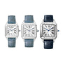 Three Cartier Santos-Dumont watches are displayed side by side, each with a square silver case, white dial, Roman numerals, blue hands, mechanical movement, and leather strap—two in light blue (left), one in dark blue (right).