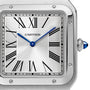 Close-up of the Cartier Santos-Dumont watch face, featuring Roman numerals, blue hands, and a sapphire-tipped crown on a brushed metal case, highlighting its refined mechanical movement.