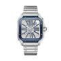 The Santos de Cartier Skeleton watch by Cartier features a silver metal band, blue bezel, exposed skeleton dial showcasing its Manufacture mechanical movement, and elegant Roman numeral markers.