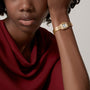 A woman in a red top, resting her head on her hand, wears the Panthère de Cartier gold wristwatch by Cartier.