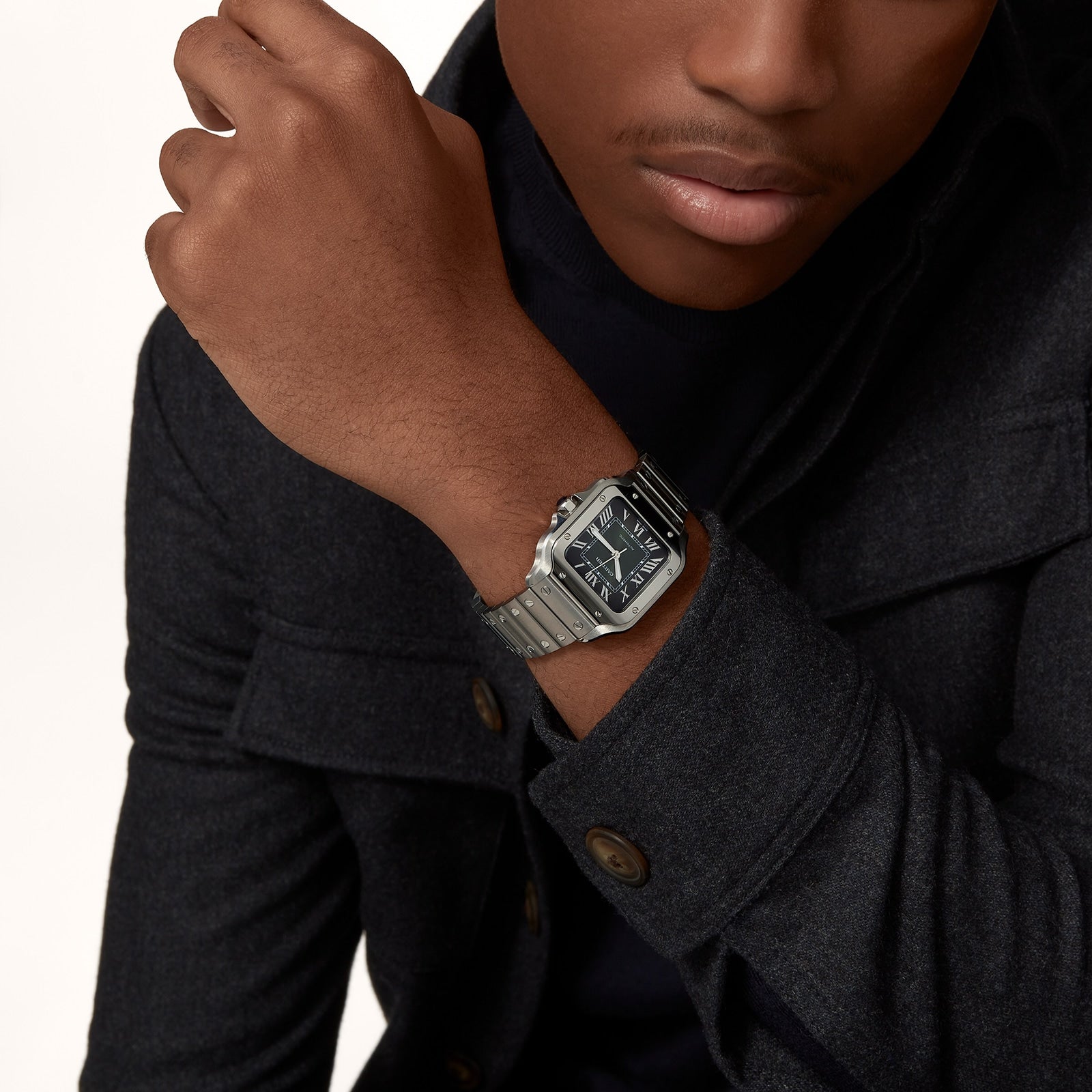 A person in a dark coat wears a Cartier Santos de Cartier silver wristwatch with a black dial, metal bracelet, and automatic self-winding movement on their left wrist.