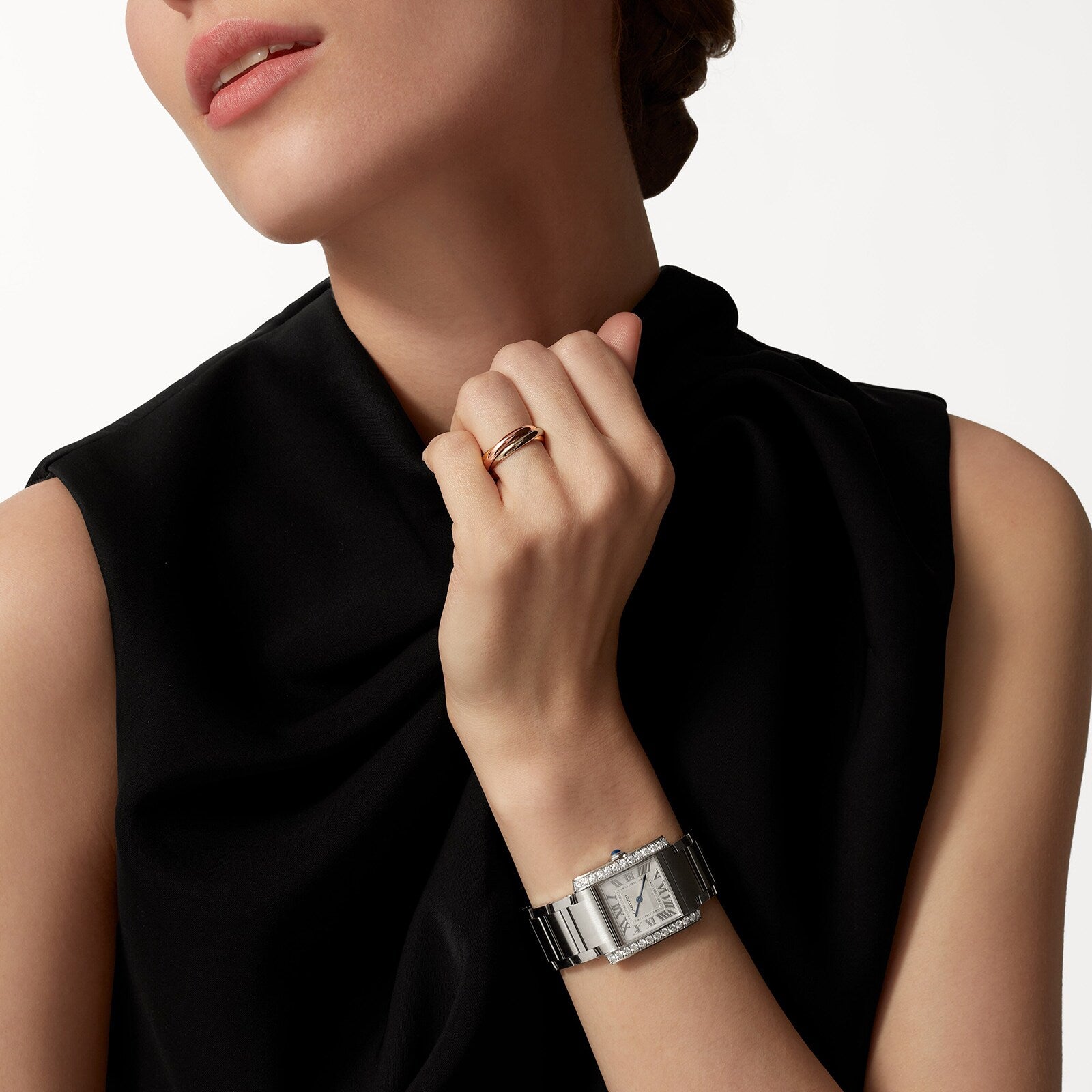 A person in a sleeveless black top and simple ring showcases the Cartier Tank Française watch on their wrist, holding their hand near their face against a plain background.