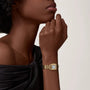 A person wearing the Panthère de Cartier Small Model by Cartier, featuring yellow gold accents, poses with their hand near their face while dressed in an off-the-shoulder black top.
