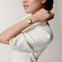 A woman in a white top showcases the Panthère de Cartier watch by Cartier, featuring a square face and 18K yellow gold, elegantly worn on her left wrist against a plain background.