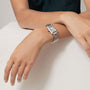 A person rests their left arm on a white surface, wearing the Cartier Tank Must de Cartier watch with a silvered dial, Roman numerals, and a sleek metal band.