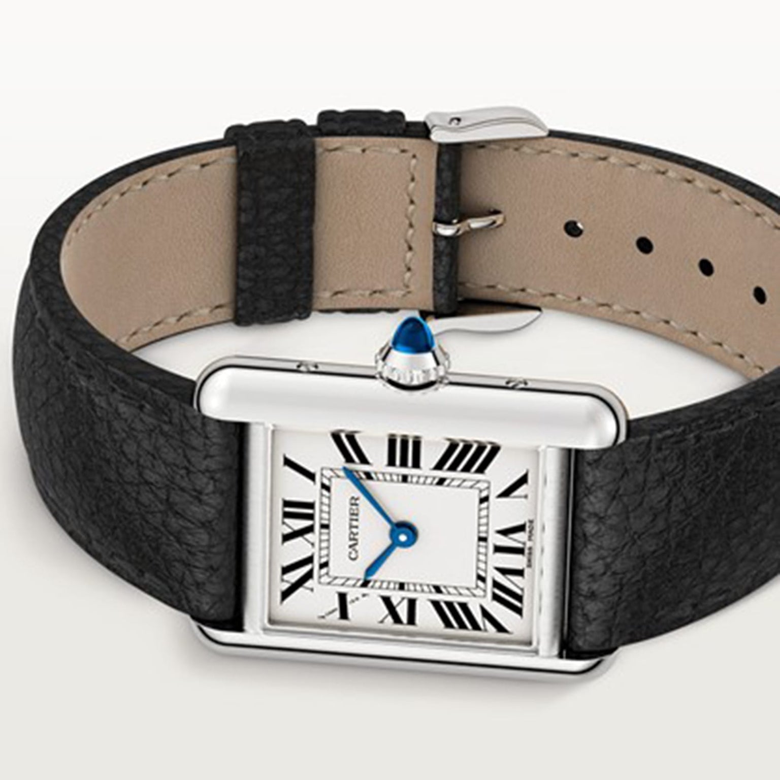 A Cartier Tank Must de Cartier watch is shown, featuring a rectangular case, white dial with black Roman numerals, blue hands, beaded crown, and a black leather strap.
