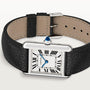 A Cartier Tank Must de Cartier watch is shown, featuring a rectangular case, white dial with black Roman numerals, blue hands, beaded crown, and a black leather strap.