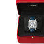 A Cartier Santos-Dumont watch with a square face and blue strap is shown in an open red Cartier box lined with black fabric.
