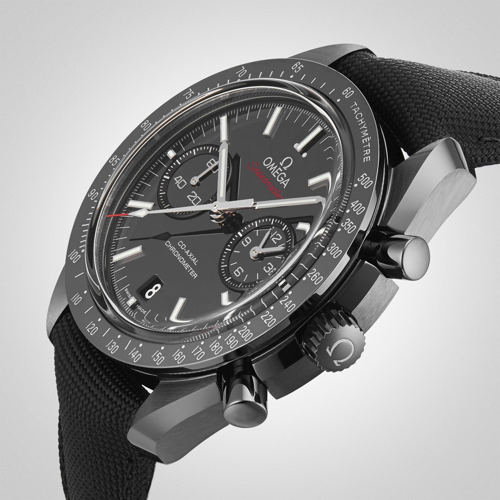 A close-up of the OMEGA Speedmaster Dark Side of The Moon Ceramic shows its black ceramic case, tachymeter bezel, chronograph subdials, and textured strap, highlighting the watch’s Lunar Legacy against a plain background.