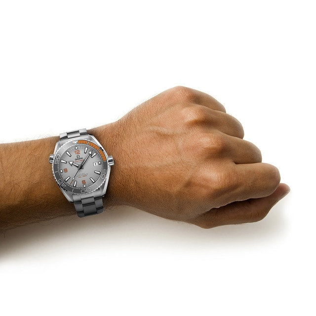 A persons wrist wearing an OMEGA Seamaster Planet Ocean 600M silver analog watch on a plain white background.
