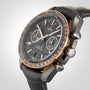 A close-up of the OMEGA Speedmaster Dark Side of the Moon Meteorite, featuring a ceramic case, black leather strap, textured dark dial with gold accents, and three subdials against a neutral background.