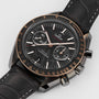 A close-up of the OMEGA Speedmaster Dark Side of the Moon Meteorite, showcasing its ceramic case, black leather strap, black and gold-accented dial with three subdials and a date window at 6 o’clock.