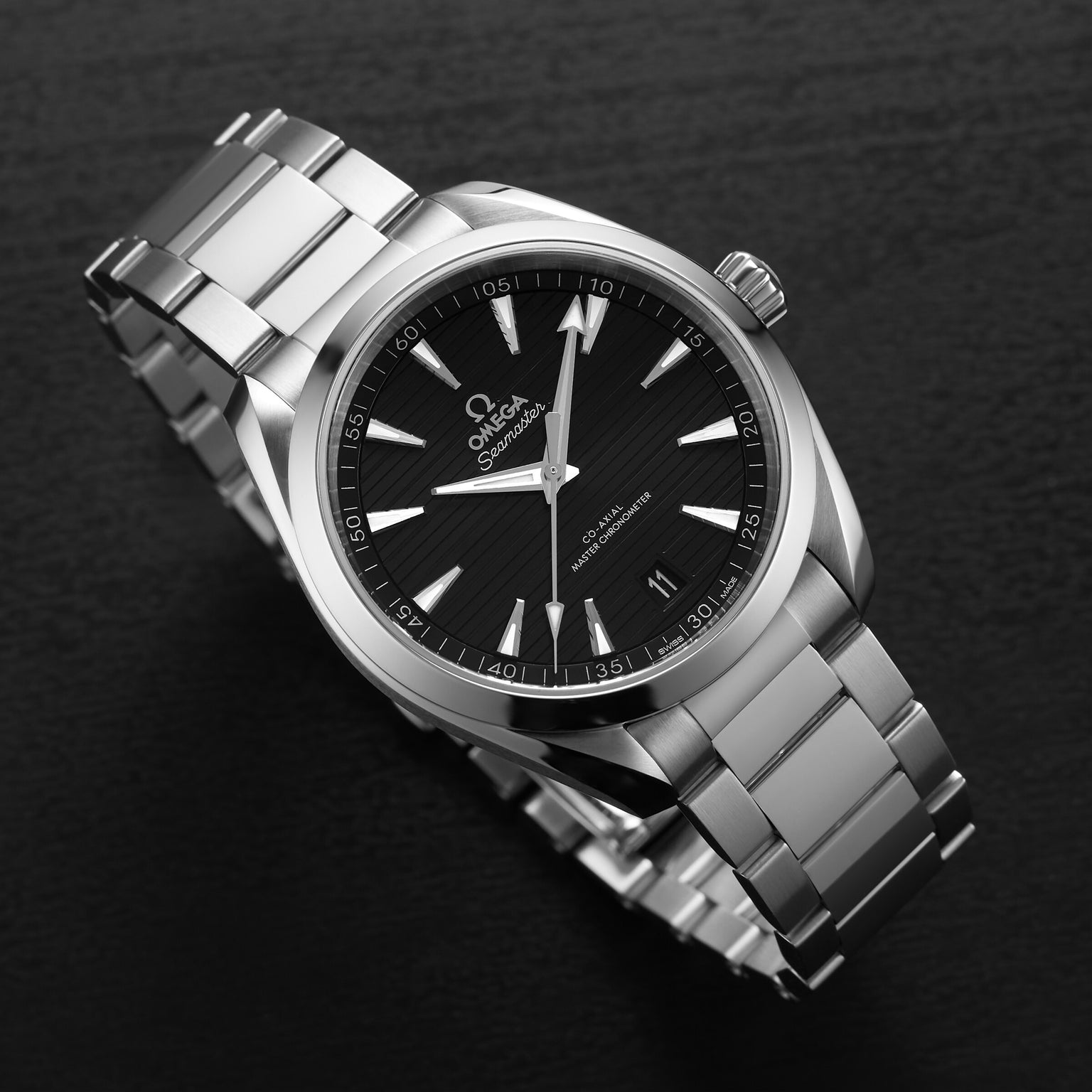 An OMEGA Seamaster Aqua Terra 150M stainless steel wristwatch with a black dial, silver hour markers, and date display—displaying the brand’s maritime heritage—is presented on a dark surface.