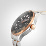 A close-up of the OMEGA Seamaster Diver 300M wristwatch with a black dial, gold and silver bezel, and metal bracelet featuring the OMEGA Co-Axial movement, set against a light background.