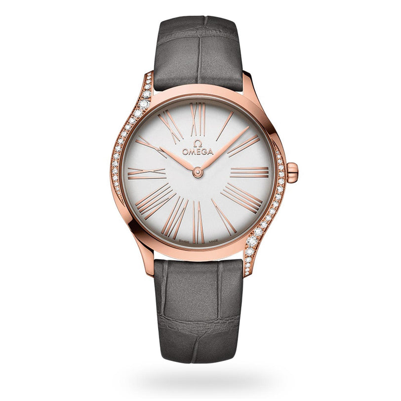 The OMEGA De Ville Tresor 36 ladies’ wristwatch in Sedna™ gold features a white dial, Roman numerals, a diamond-studded bezel, and a grey leather strap, displayed elegantly against a white background.
