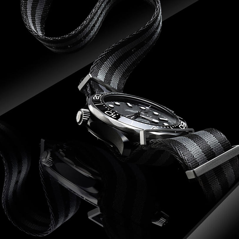 A close-up of the OMEGA Seamaster Diver 300M, a black and silver dive watch with a black and gray striped nylon strap, displayed on a reflective black surface.