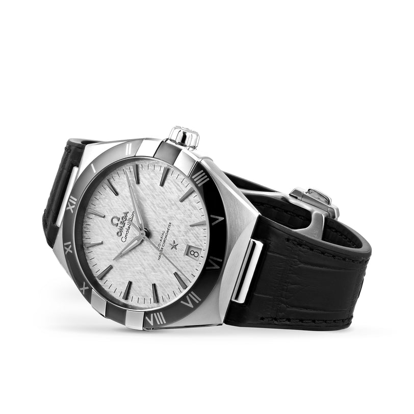 An OMEGA Constellation stainless steel watch with Master Chronometer 8900 Calibre, textured white dial, black Roman numeral bezel, date display, and black leather strap is angled on a white background.