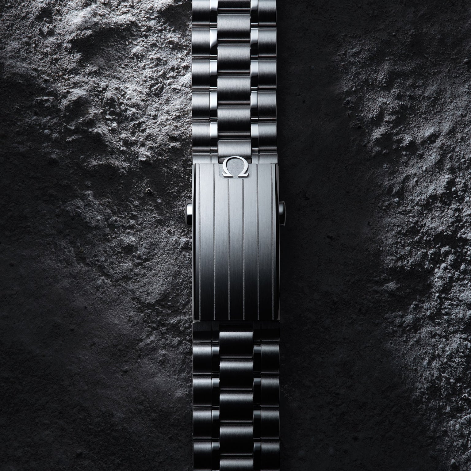 The OMEGA Speedmaster Moonwatch Professional’s metal bracelet, featuring the iconic logo on its clasp, is displayed vertically on a textured, stone-like surface—a tribute to its legendary legacy.