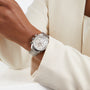 A person wearing a cream-colored blazer displays an OMEGA Speedmaster 38 on their left wrist.