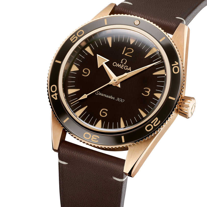 An OMEGA Seamaster 300 wristwatch with a bronze gold case, brown dial, brown leather strap, and rotating bezel is displayed at an angle against a white background.