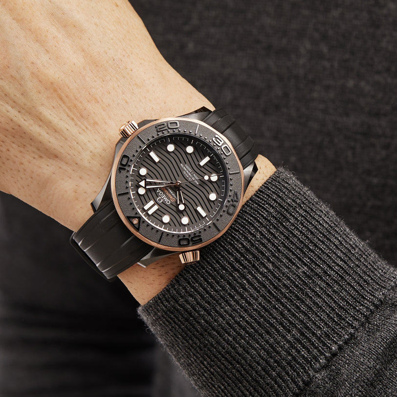 A person sports an OMEGA Seamaster Diver 300M wristwatch with a black and silver case, rubber strap, and textured dial, paired with a dark sweater—a classic tribute to the iconic James Bond timepiece.