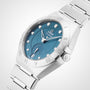 The OMEGA Constellation features a 34mm silver case, blue dial with diamond hour markers, Roman numeral bezel, and a metal link bracelet, displayed at a slight angle.