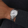 A person wearing an OMEGA Seamaster Aqua Terra 150M silver wristwatch with a white face and metal band on their left wrist, dressed in a dark gray sweater.