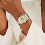 A person wearing an OMEGA Seamaster Aqua Terra 150M wristwatch with a beige dial and metallic band, dressed in an off-white blazer.