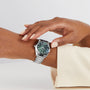 A person with light-colored nail polish and a cream sleeve adjusts their OMEGA Seamaster Aqua Terra 150M, a silver watch with a green dial and 8802 calibre movement, on their left wrist.