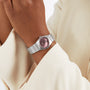 A person in a beige jacket showcases an OMEGA Constellation silver wristwatch with a blush rose dial and stainless steel bracelet on their left wrist.