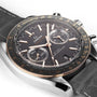 OMEGA Speedmaster Racing wristwatch featuring a black dial, gold accents, and a black leather strap shown on a white background.