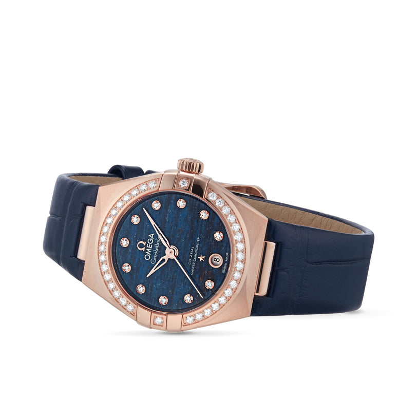 The OMEGA Constellation is a luxury wristwatch with a blue strap, 18K Sedna™ gold case, diamond-set bezel, blue Aventurine stone dial, and diamond hour markers. It exudes elegance and is shown on a white background.