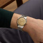A person in a dark green long-sleeve shirt wears an OMEGA De Ville Prestige wristwatch featuring a Moonshine Gold dial and date display.