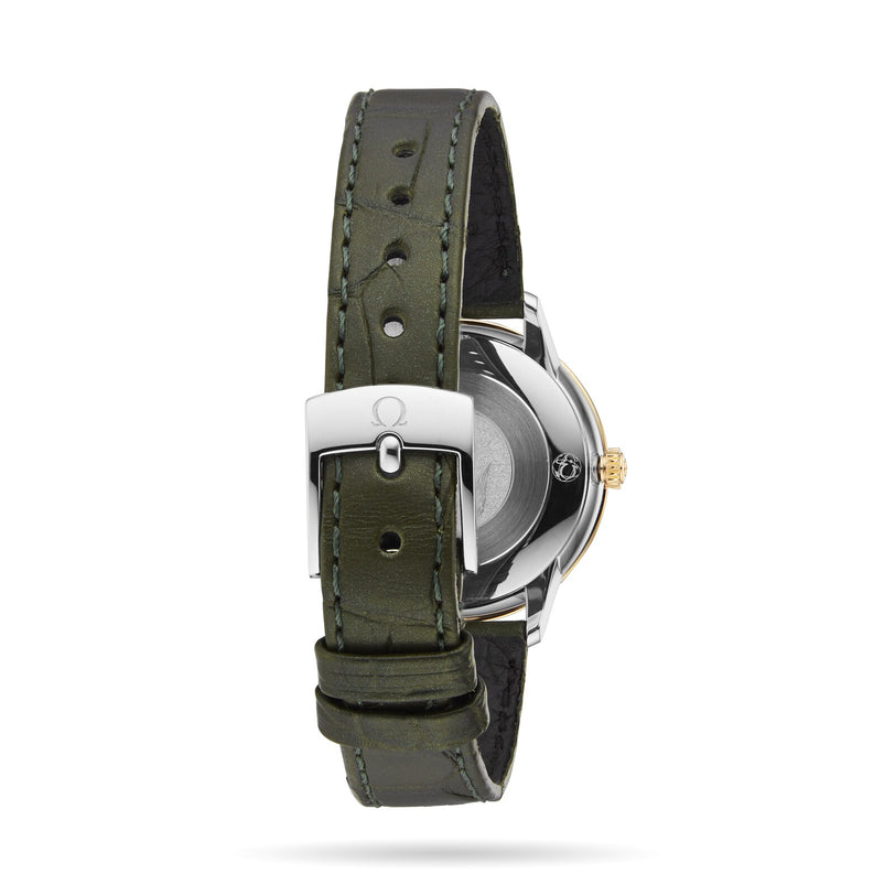 A close-up of the OMEGA De Ville Prestige wristwatch showcases its green leather strap, silver buckle, and partially visible stainless steel and 18K yellow gold case.